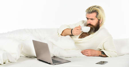 Screen Time and Insomnia. Happy hipster drink coffee in bed. Bearded man enjoy coffee and surfing...