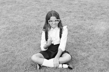 Stay focused. Unhappy girl wear prop glasses. Beauty look of fashion model. Little child wear school uniform. Back to school fashion. Small fashionista green grass. Fashion accessory. Fashion styleの写真素材