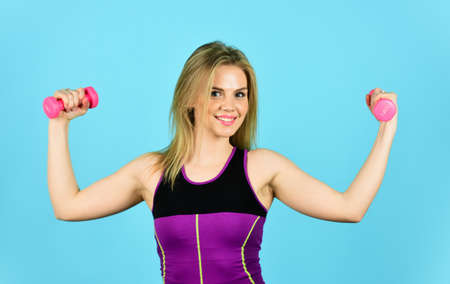 Great progress. Slim girl doing triceps exercise with dumbbell in the gym. coach dressed in sport clothes. muscular woman in training pumping up muscles of hands. girl use barbell blue backgroundの写真素材