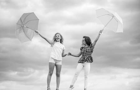 Weather forecast. Weather changing. Carefree children outdoors. Ready for any weather. Girls friends with umbrellas cloudy sky background. Windy or rainy we are prepared. Freedom and freshnessの写真素材
