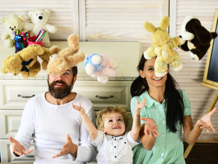 Mom, dad and boy throw toys up on wooden background.