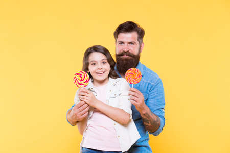 Sweet dessert concept. Bearded hipster good daddy for adorable daughter. Daughter and father eat sweet candies. Sweet childhood. Lovely surprise. Girl cheerful child and dad hold colorful lollipopsの写真素材