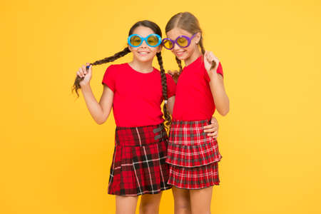 Summer fashion trend. Summer fun. Summer accessory. Girls cute sisters similar outfits wear colorful sunglasses for summer season. Kids fashionable friends posing in sunglasses on yellow backgroundの写真素材