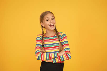 Goods for teens. Adorable girl beautiful face. Little girl. Small child with cute braids hairstyle on yellow background. Child care concept. Preteen girl colorful clothes. Childrens shop store mallの写真素材
