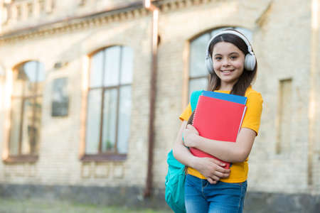 smiling kid hold folders. childhood happiness. girl in headset listen music. get knowledge from ebook. modern school education. back to school. happy teen carry workbookの写真素材