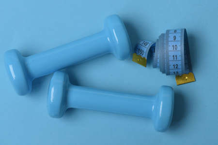 Dumbbells made of plastic and measure tape on cyan background