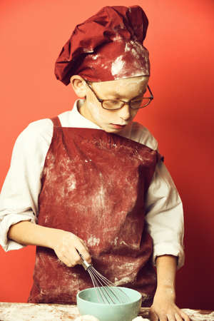stained cute cook chef boy on red studio background.