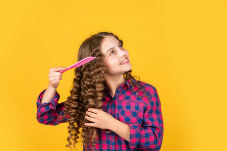 Hairstyle for party. Hairdresser supplies. Fashion and beauty. Small girl hairdresser salon. Brushing long hair. Enjoying shiny curls. Balm oil conditioner for styling. Little child curly hairの写真素材