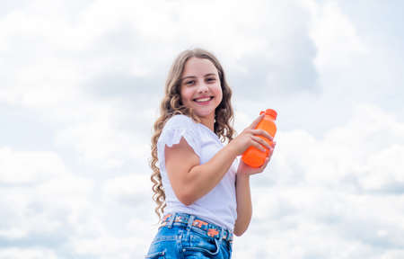 She is really cute. child hold bottle of water. Child on the background of sky. summer holiday concept. childhood happiness. happy childrens day. drinking fresh juice. kid beauty and fashionの写真素材