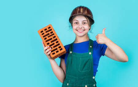 best quality. happy childhood. kid wear protective helmet. protect head on construction site. teen girl hold brick. little builder with brick. child is engineer architect. building her future houseの写真素材