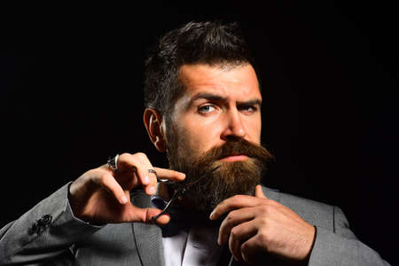 Man with beard holds steel scissors. Businessman with serious face