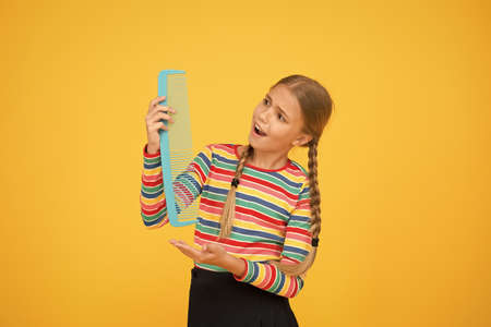Professional equipment. Combing hair. Cheerful happy smiling little kid with giant comb. Comb for tangled hair. Hairdresser supplies. Large comb. Girl long hair hold enormous comb. Hairdresser salonの写真素材
