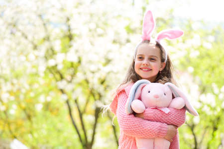 Holidays celebration concept Easter and spring. Happy girl holding pink rabbit in garden with blossoming trees.の写真素材