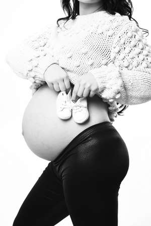 female hands of pregnant woman holding baby booties on bellyの写真素材