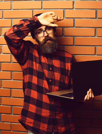 Bearded brutal caucasian hipster holding laptop on brown brick wall studio backgroundの写真素材