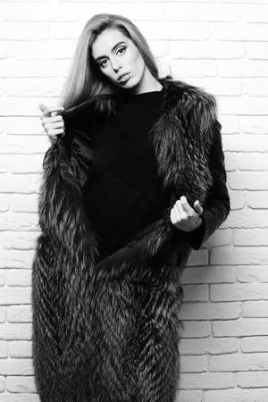 fashionable sexy woman in fur on white brick wall studio backgroundの写真素材