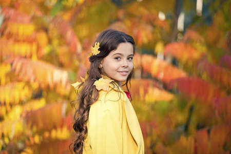 Adorable smiling schoolgirl autumn foliage background. Good mood. Happy child. Enjoying every season. United with nature. Little child walk in autumn park. Autumn season leisure. Atmosphere of autumnの写真素材