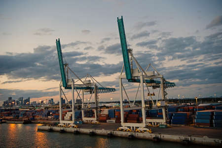 Miami, USA - March 01, 2016: cargo cranes on cloudy sky. Containers in cargo port. Waterfront cargo loading equipment. Cargo shipping. Evening city skylineのeditorial素材