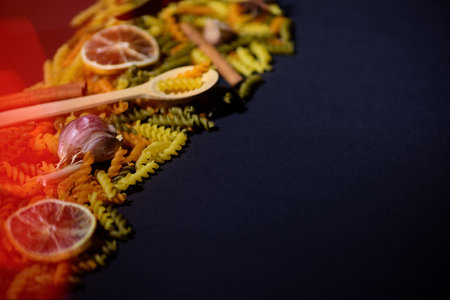 delicious colorful pasta with spoon, chili pepper, orange, garlic and cinnamon on dark background, copy spaceの写真素材