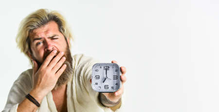 Awakening concept. Insomnia sleep disorder. Healthy habits and lifestyle. General recommendations for sleep. Stressed man alarm clock. Sleepy guy and alarm clock in bed. Bearded man with alarm clockの写真素材