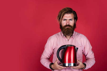 bearded man shop assistant presenting kitchen utensil. useful in housekeeping. mature charismatic male use electric kettle. guy with beard and moustache make tea. drink hot tea. copy spaceの写真素材