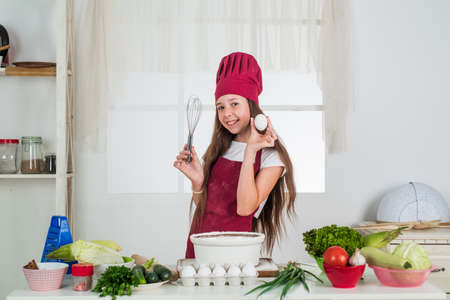 dieting. happy childhood. happy child wear cook uniform. chef girl in hat and apron. kid cooking food in kitchen. choosing a career. little helper with beater and egg. culinary and cuisineの写真素材