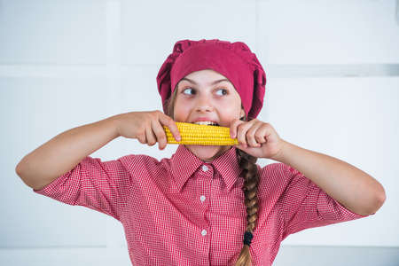 having strong teeth. healthy and organic food only. full of vitamins. kid wear chef uniform and hat. teen girl biting corn. fresh raw vegetables. time to eat. happy child cooking in kitchenの写真素材