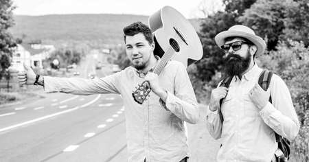 Men try stop car thumb up. Travel by autostop. Hitchhiking cheapest ways traveling. Hitchhiker meet friend. Travelers with backpack and guitar ready strat new journey. Looking for transportの写真素材
