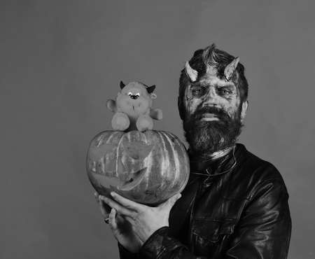 Man wearing scary makeup holds pumpkin and red devil toyの写真素材