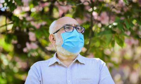 enjoy the beauty. man at sakura in protective mask. smell blooming flowers on coronavirus quarantine. observe precautions while pandemic. healthy life. wear mask in blossoming pink sakura parkの写真素材