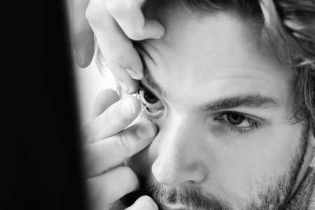 Man with beard and blue eyes puts contact lenses onの写真素材