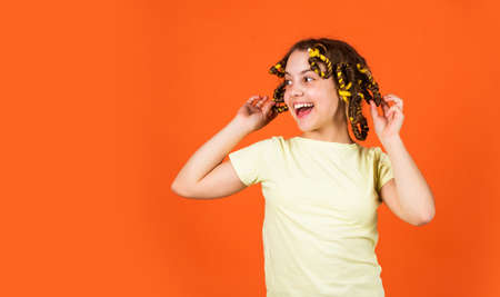 Styling tips. Small girl Curling Hair Using Curlers orange background. Adorable child hairdo. Teen...