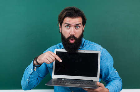 surprised mature teacher working on computer. brutal bearded man work in classroom with laptop....