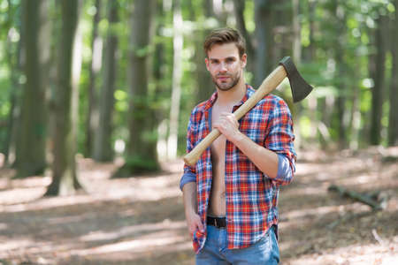 lumberjack man in open plaid shirt with jeans carry large splitting axe in summer forest natural landscape, woodの写真素材