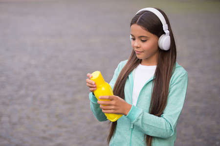 kid in earphones open water bottle to drink because of thirst, healthy lifestyle