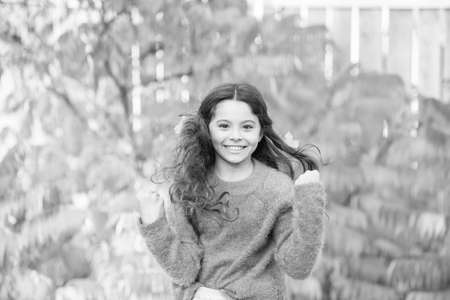 Wind in her hair. Happy little child with colorful leaves in long brunette hair. Autumnal look of...