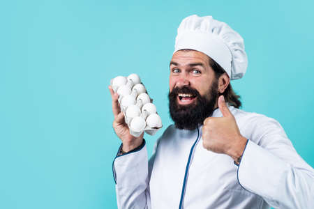 confident chef guy with beard and moustache in cook uniform show thumb up for healthy eggs, natural foodの写真素材