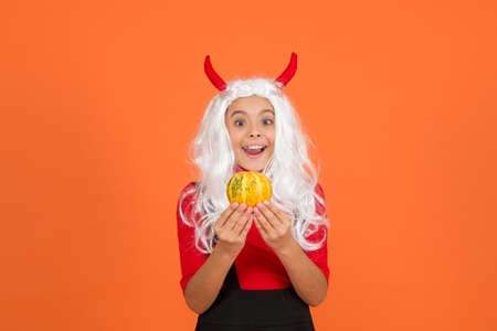 surprised child celebrate autumn holiday with traditional food. teenage girl in devil horns celebrate halloween. happy halloween. trick or treat. carnival festive costume of witch. kid with pumpkinの写真素材