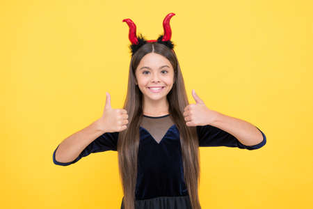 kid wear devil horns show thumb up. childhood autumn holiday. funny teen girl ready to celebrate party. costume party fun. happy halloween. child in imp horns. perfect partyの写真素材