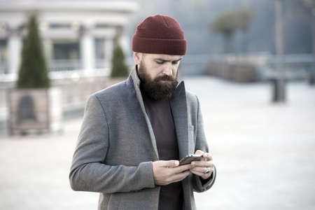 Fashion man with beard. brutal caucasian hipster with moustache. Bearded man. Mature hipster with beard. Male barber care. man typing message on smartphone. be online. call the taxi.の写真素材