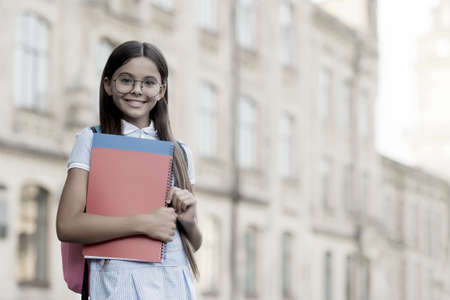 Happy smart kid wear glasses back to school carrying backpack and books at education building outdoors vintage filter, retro, copy spaceの写真素材