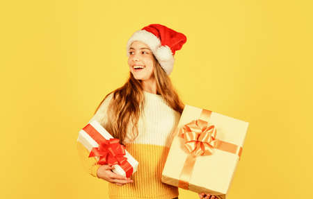 christmas shopping online. time for discount. smiling kid hold purchase. presents and gifts from santa claus. small girl santa at yellow background. xmas party celebration. happy new yearの写真素材