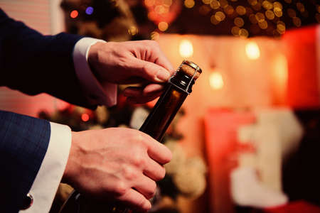 Open champagne and celebrate holiday. Celebrate new year with champagne drink. Toast and cheers concept. Male hands opening champagne bottle on christmas decorations background. Lets celebrateの写真素材