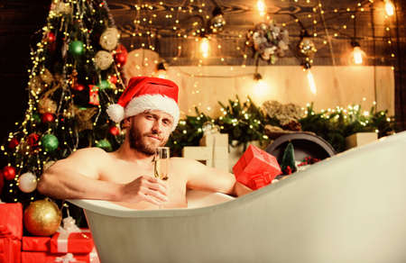 Winter holidays. New year. Mature man lying in bathtub drink champagne. Spa and wellness. Hot bath. Hot bath health benefits. Santa Claus luxuriate in warm bath. Take delight. Pampering myselfの写真素材