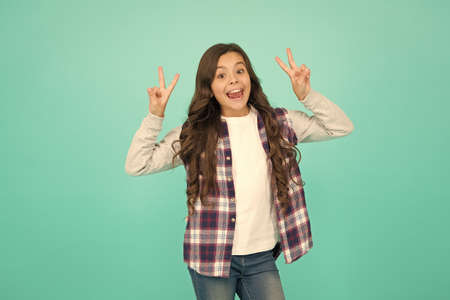 Peace to everybody. Cute girl with long hair. Small girl checkered shirt. Happy international childrens day. Little girl turquoise background. Good mood concept. Positive vibes. Sincere emotionsの写真素材