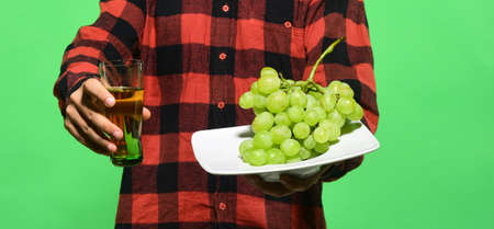 Guy shows harvest. Male hands hold glass of grape juice