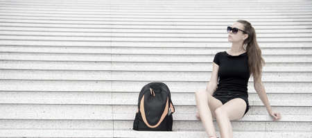 Girl tourist relaxing on stony stairs near her backpack. Take minute to relax. Woman sunglasses stylish black outfit walking Paris. Vacation and travel concept. Low cost tour explore Europeの写真素材