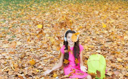 I would stay here forever. back to school. concept of online education. child sit in autumn leaves. girl in earphones with school bag. kid listen music in autumn park. fall is a time for studyの写真素材