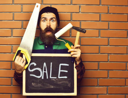 bearded worker holding various building tools and board, surprised faceの写真素材