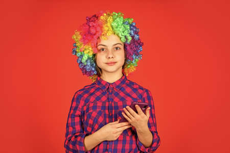 small girl colorful wig use smartphone. positive and cheerful. childhood happiness. kid looking funny in rainbow wig hair. hair dyeing at hairdresser. child having fun. happy birthday partyの写真素材